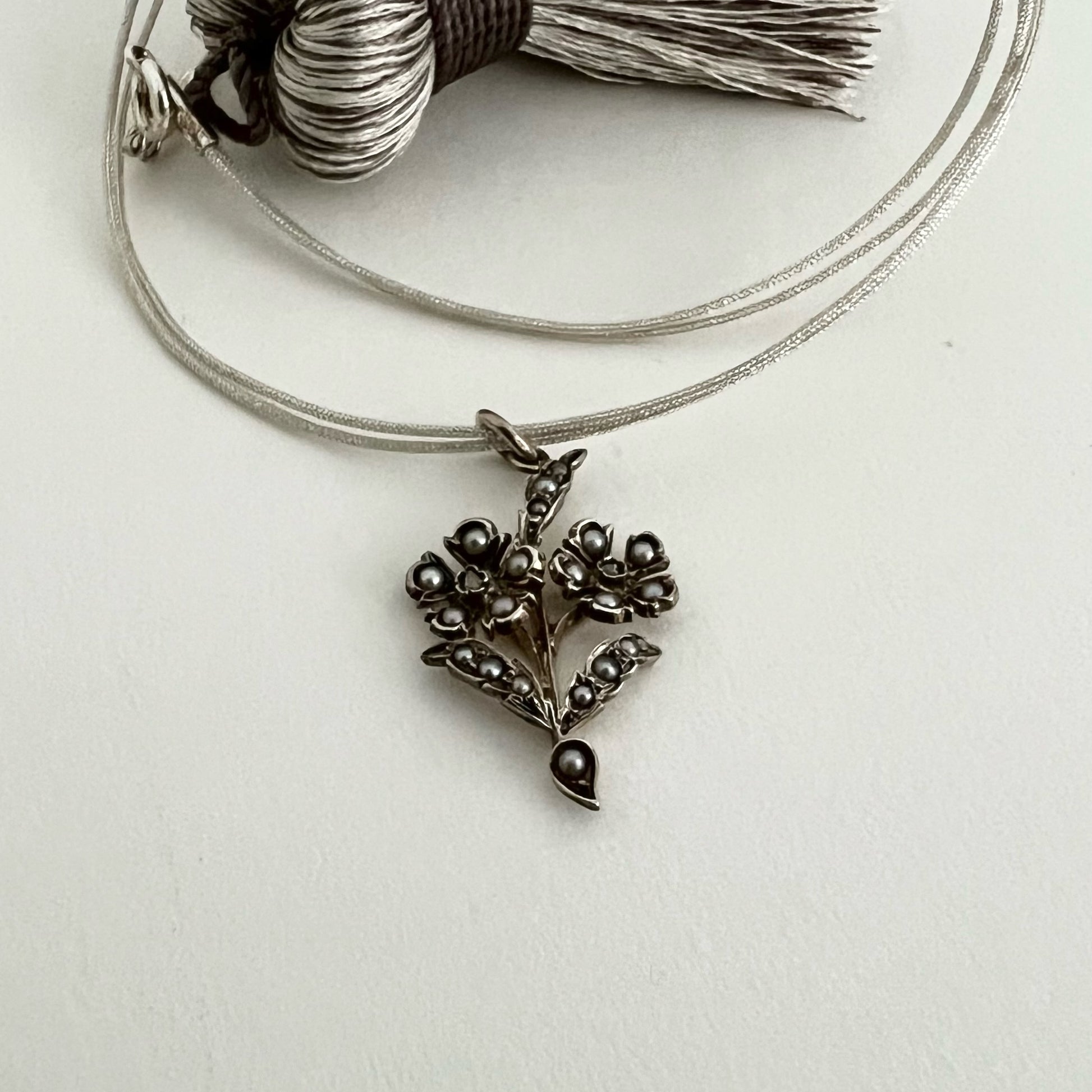 Small bouquet of flowers, antique silver and gold pendant, pearls and rose-cut diamonds with a necklace made from a double strand of grey Japanese silk thread.